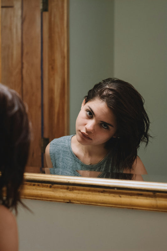 Person checking their hair in a bathroom mirror under natural light